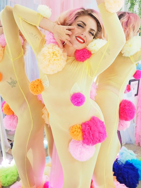 Lou P in yellow catsuit with colourful pompoms on it